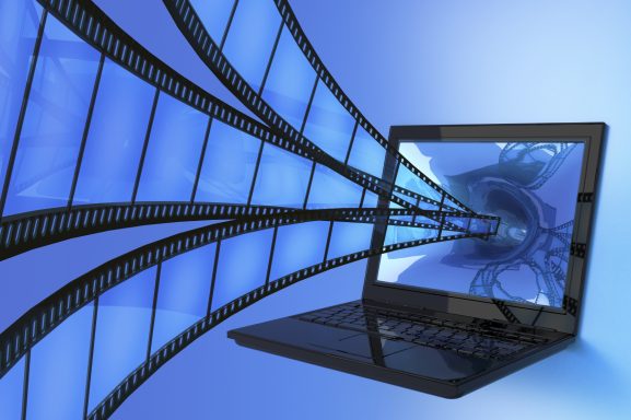 Ein Laptop mit filmähnlichen Strahlen in Blau, die aus dem Bildschirm strömen.
