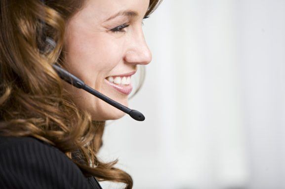 Frau mit Headset, lächelnd, in einem Bürosetting.