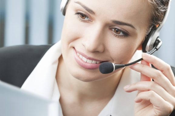Junge Frau mit Headset, die freundlich am Computer arbeitet und telefoniert.