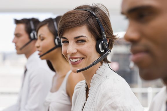 Lächelnde Frau mit Headset, Teil eines Teams im Kundenservice.