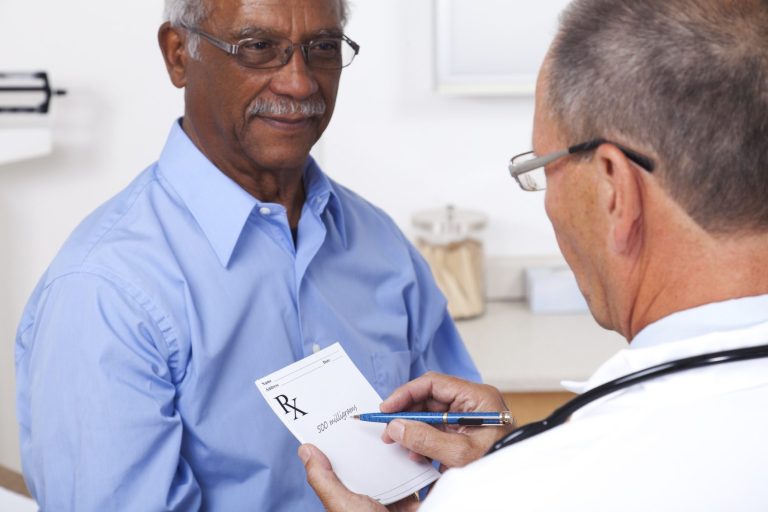 Älterer Mann in Arztpraxis, Doktor schreibt Notizen auf einer Karte.