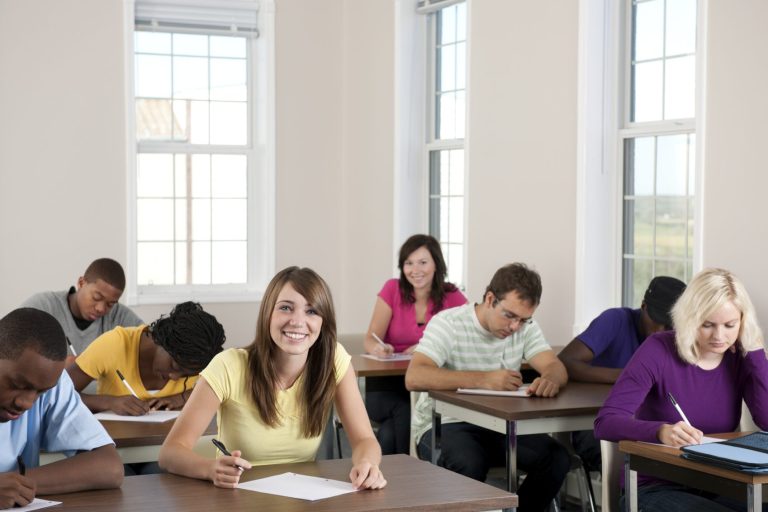 Sechse Studierende in einem Klassenraum, einige schreiben, andere schauen nachdenklich.